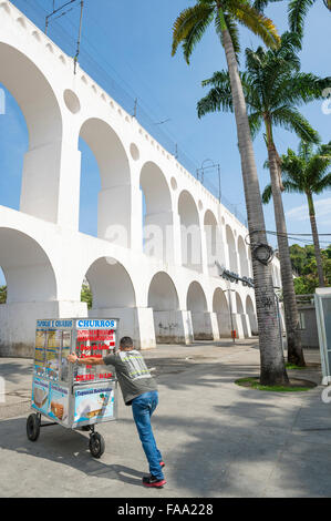 RIO DE JANEIRO, Brasilien - 22. Oktober 2015: Brasilianische Straße Verkäufer schiebt einen Lebensmittel-Wagen mit Churros Snacks unter Lapa Bögen Stockfoto