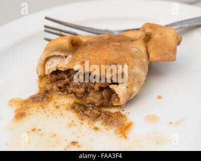 Die Hälfte gegessen empanada auf weißer Teller mit Gabel hinter das Essen. Fleisch auf dem Teller verteilen, und sieht in der Farbe warm und würzig im Geschmack. Stockfoto