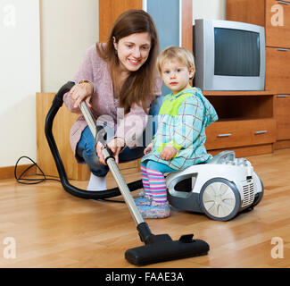 Glückliche Hausfrau mit einem Kleinkind, Wohnzimmer mit Staubsauger reinigen Stockfoto