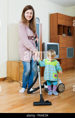 Junge Mutter mit ihrem Kind tun home Reinigung mit einem Staubsauger Stockfoto