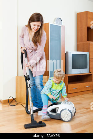 Lächelndes Mädchen mit Baby Reinigung Wohnzimmer mit Staubsauger Stockfoto