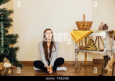 Einsames Mädchen sitzt hinter Weihnachtsbaum mit präsentiert Stockfoto