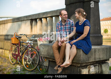 Paar mit Fahrrädern sitzt auf einer steinernen Damm. Stockfoto