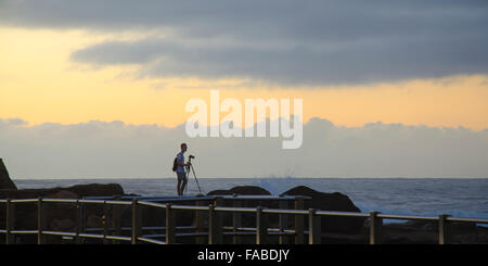Ein Einzelfotograf steht an der felsigen Küste, während er das Morgenlicht an einem Strand in Sydney in Australien einfängt Stockfoto