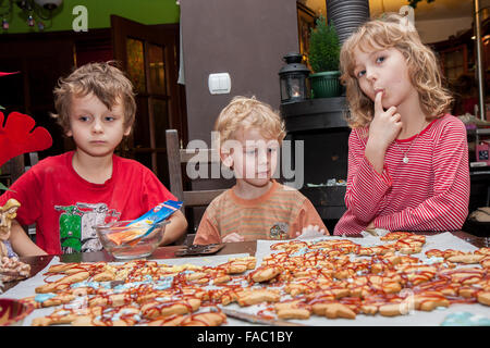 Drei kleine Kinder sitzen an einem Tisch und festliche Dekoration Ingwer Cookies mit Zuckerguss. Stockfoto