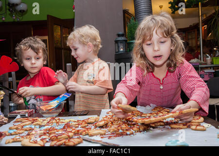 Drei kleine Kinder sitzen an einem Tisch und festliche Dekoration Ingwer Cookies mit Zuckerguss. Stockfoto