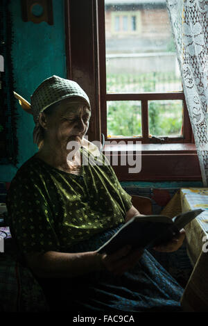 Ältere Frau liest ein Buch am Fenster im Kreis Maramures, Rumänien Stockfoto