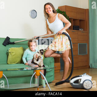 Junge, lächelnde Mutter und Töchterchen Wohnzimmer mit Staubsauger reinigen Stockfoto