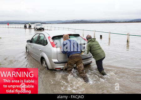 Eine Autofahrer stecken in Hochwasser auf der Straße zu Storth an der Mündung der Kent in Cumbria, UK, während der Januar 2014 Sturmflut und hohen Gezeiten wird von zwei Helfern herausgeschoben. Stockfoto