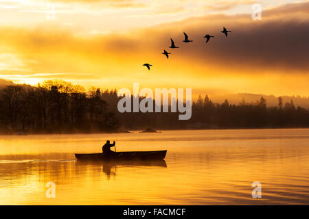 Sonnenaufgang über dem Lake Windermere in Ambleside, Lake District, Großbritannien, mit einem Mann ein kanadisches Kanu paddeln. Stockfoto