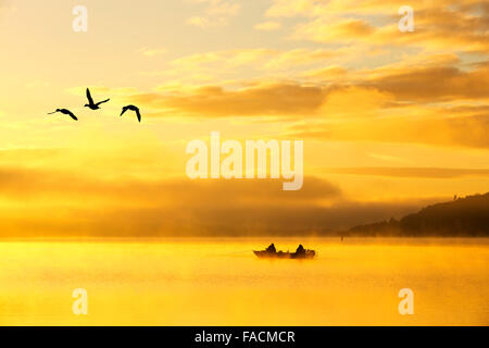 Sonnenaufgang über Männer Angeln in einem Boot auf dem Lake Windermere in Ambleside, Lake District, Großbritannien. Stockfoto