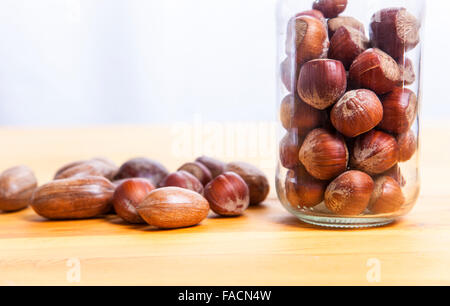 Pecan-Nüssen und Haselnuss auf Glas jar über Holzoberfläche. Isoliert auf weißem Hintergrund Stockfoto