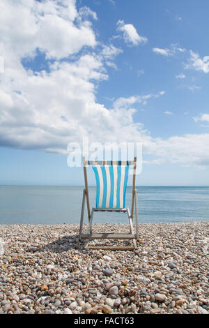 Einzigen blau-weiß gestreiften Liegestuhl mit Blick auf den Ozean auf einem Kiesstrand. Stockfoto