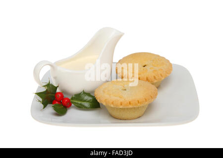 Zwei Blatt vor den Mund Pis auf einem Teller mit einem Krug Creme und ein Zweig der Stechpalme auf einem Teller isoliert gegen weiß Stockfoto