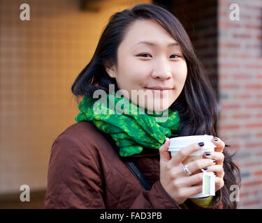 Junge asiatische Frau lächelt in die Kamera, während ihre Hände mit Tee in einen Pappbecher in den Winter-Straßen von Manhattan. Stockfoto