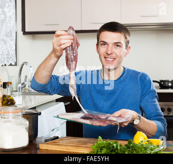 Gewöhnliche lächelnder Mann mit roher Tintenfisch in Küche zu Hause Stockfoto