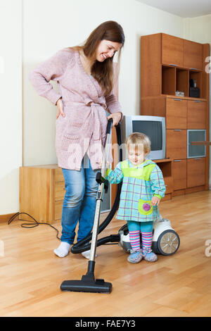 Glücklich lächelnde junge Mutter mit kleinen Tochter Reinigung mit Staubsauger Stockfoto