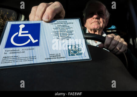 Älteren Mann setzen EU-Parkausweis für Menschen mit Behinderungen – Blue Badge - hinter der Windschutzscheibe des Autos behindert Stockfoto