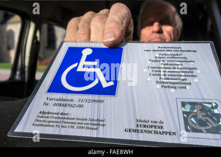 Älteren Mann setzen EU-Parkausweis für Menschen mit Behinderungen – Blue Badge - hinter der Windschutzscheibe des Autos behindert Stockfoto