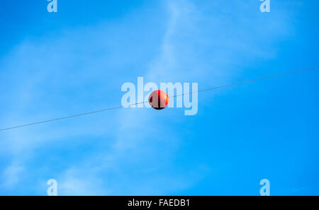 Einzelne orange Sicherheit Gefahr Warnung Ballmarker auf Metall Einzelkabel gegen blau-weißen Himmel. Stockfoto