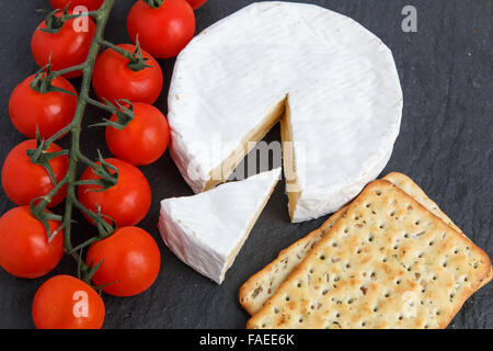 Brie Weichkäse mit Crackern und Tomaten auf einem grauen Schiefer Brett. Stockfoto