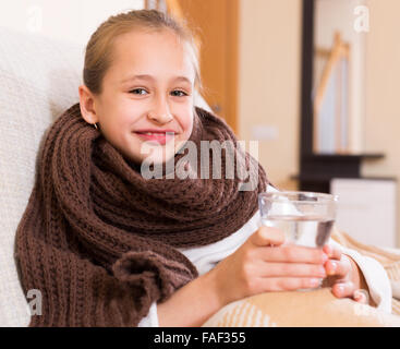 Lächelnd Schulmädchen gekleidet in warmer Schal aus Glas auf der Couch zu Hause trinken Stockfoto