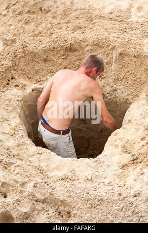 Mann, der im August ein tiefes Loch in den Sand am Bournemouth Beach, Bournemouth, Dorset UK gräbt Stockfoto