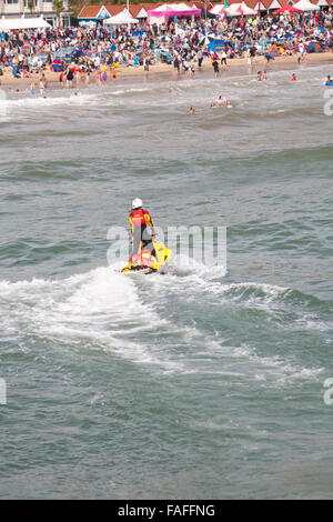 RNLI-Rettungsschwimmer Jetski mit Rettungsschwimmer standen an einem warmen, sonnigen Tag im August auf See auf Patrouille am überfüllten Bournemouth Beach, Bournemouth, Dorset UK Stockfoto