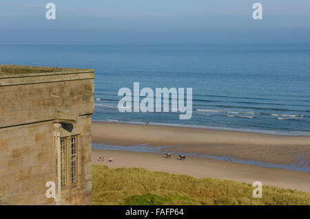 Reiten Bamburgh Strand entlang betrachtet von Bamburgh Castle. Northumberland. England. VEREINIGTES KÖNIGREICH. Europa Stockfoto