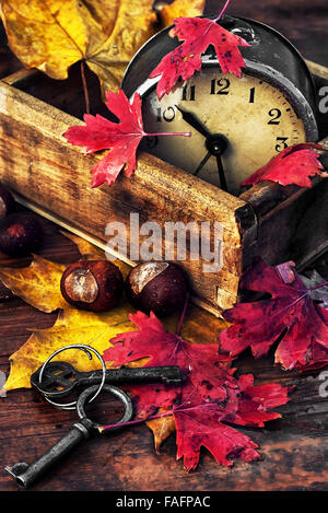 Veraltete Wecker auf hölzernen Hintergrund übersät mit abgefallenen Blättern Stockfoto
