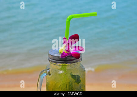 Große Gläser Becher Stil vollen Glas frisch gefrorenen Mojito mit Metallkappe Deckel, Stroh und lila Orchidee Blume im Café am Strand Stockfoto