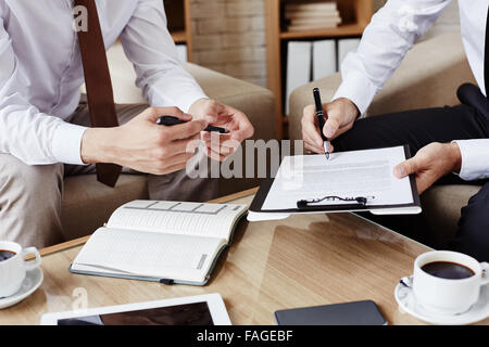 Männliche Mitarbeiter mit Stift auf Vertrag während seiner Partnerin zu zeigen, wo zu unterzeichnen Stockfoto