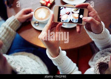 Mädchen hält Smartphone mit Foto von zwei Tassen Kaffee Stockfoto