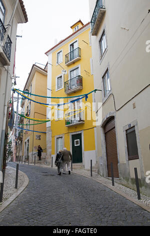 Die Menschen gehen über die schmale Straße mit gelben Häuser in Lissabon Portugal Stockfoto