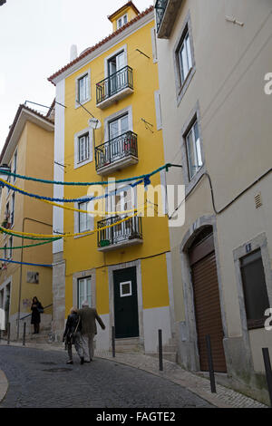 Die Menschen gehen über die schmale Straße mit gelben Häuser in Lissabon Portugal Stockfoto