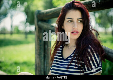 Junges Mädchen mit Strohhut sitzt auf einer Holzbrücke in einem Park im Frühjahr Stockfoto