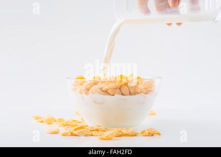 Glas Milch wird in Cornflakes Schüssel gegossen wird. Stockfoto