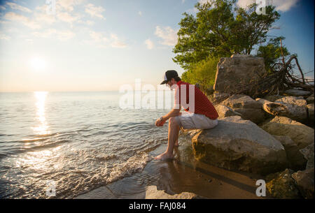 Nachdenklicher Mann sitzt auf einem Stein vom Seeufer. Punkt Pelee, Ontario. Stockfoto