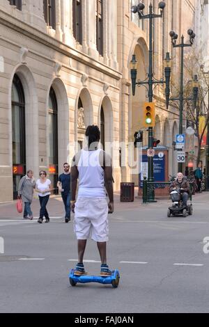 Junger Mann reitet auf einem motorisierten Hoverboard auf einer Stadtstraße Zentrum in Calgary, Alberta, Kanada. Stockfoto