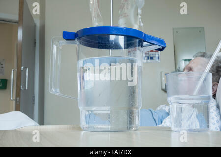 Ältere Dame in ihre neunziger Jahre im Bett auf NHS Krankenstation mit Krug Wasser auf den Nachttisch. Stockfoto