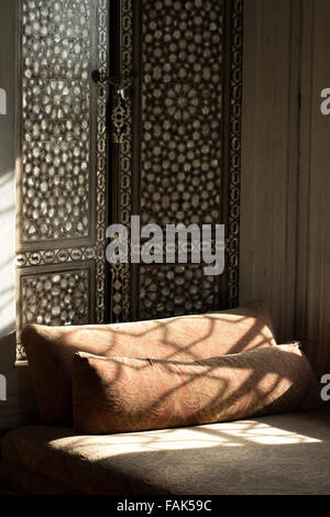 Harem-ähnlichen Ansicht mit Bett mit ziegelroten Kissen und Licht aus einem geschmückten Fenster in arabischem Stil Stockfoto
