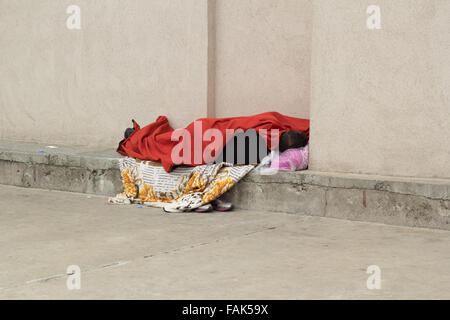 Obdachloser schlafen, bedeckt mit Kleidung Stockfoto