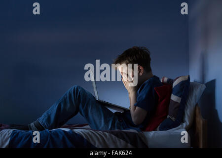 Online-Mobbing, Cyber-Mobbing Foto eines verärgert jungen in seinem Schlafzimmer Blick auf verletzende Nachrichten auf social media Stockfoto