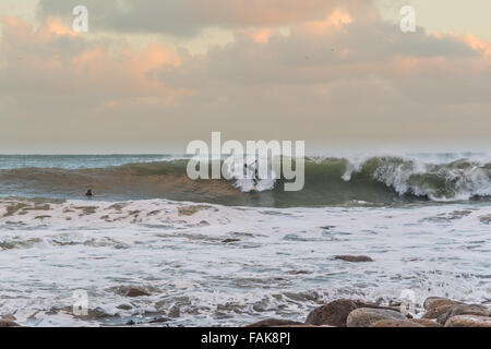 Mousehole, Cornwall, UK. Großbritannien Wetter. 31. Dezember 2015. Surfer genießen das Endstückende des Sturm Frank, bei Sonnenuntergang am Silvester in Mousehole. Bildnachweis: Simon Yates/Alamy Live-Nachrichten Stockfoto