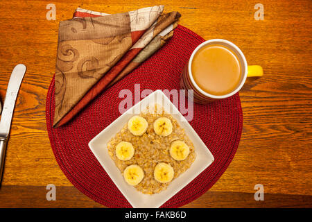 Eine Schüssel Haferflocken mit Bananenscheiben und Zimt auf ein rundes Platzdeckchen auf einem Holztisch Stockfoto