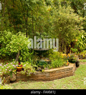 Angelegter Garten mit reich verzierten Brunnen / Wasser-Funktion, die umgeben von Steinmauer, dichten Sträuchern, Bäumen, bunten Blumen und Rasen in Australien Stockfoto