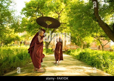 Zwei kleine buddhistischen Novizen walking im Freien im Schatten der grünen Baum vor Kloster, Myanmar. Stockfoto