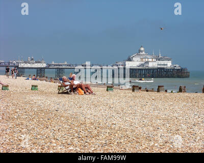 alte Damen sitzen auf Stühlen Decks auf Eastbourne Strand mit Badesteg im Hintergrund Stockfoto