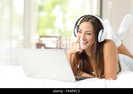 Mädchen mit Kopfhörern hören der Musik in einem Laptop auf dem Bett zu Hause Stockfoto