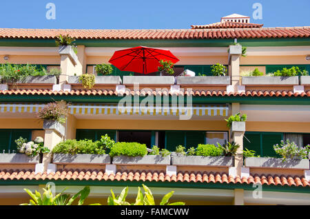 Sonnendurchflutetes mehrstöckigen orangefarbenen und grünen Reihenhaus mit roten Dach Pflanzen wachsen an sonnigen Tag, Spanien Stockfoto